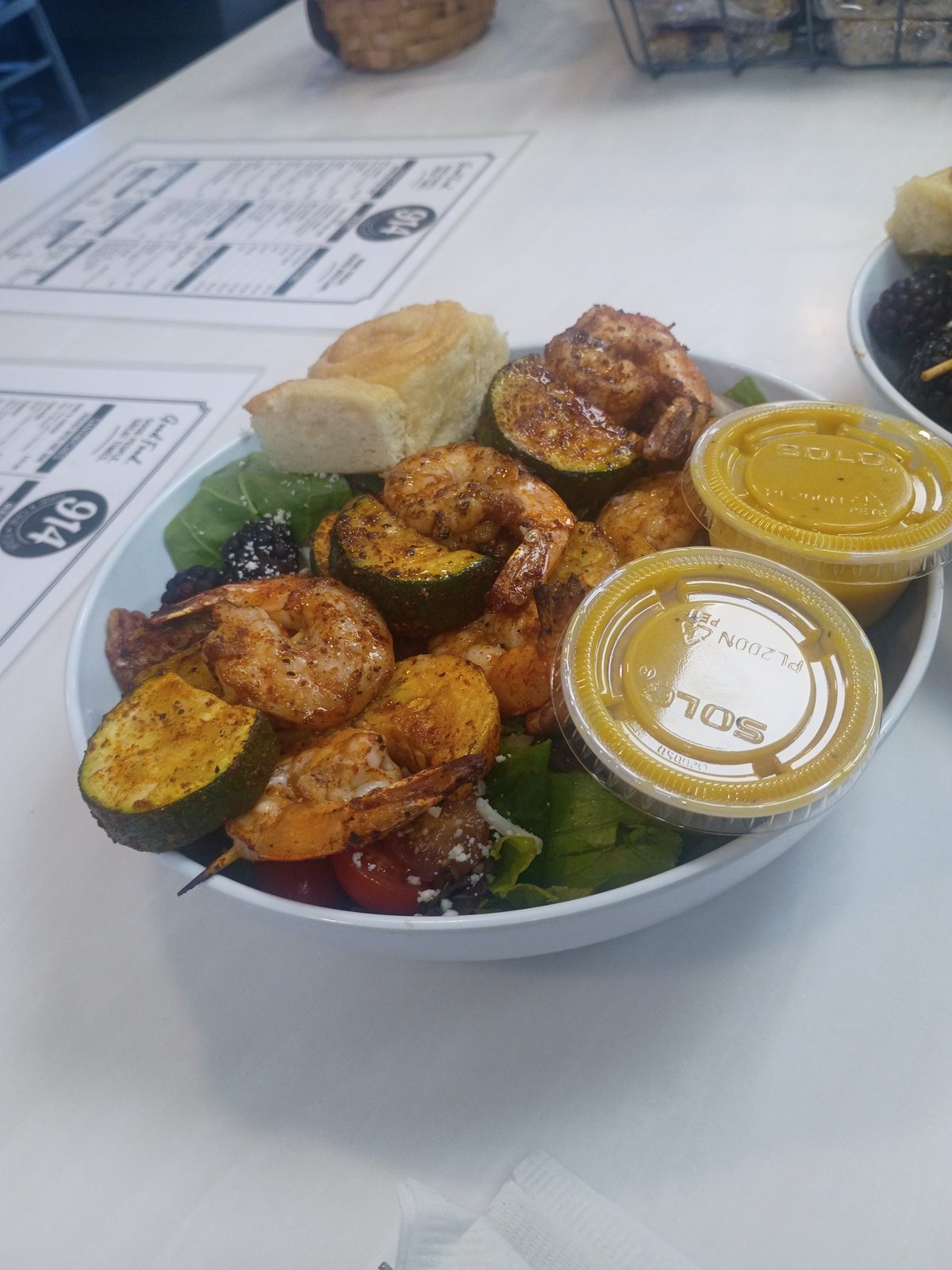 A salad topped with seasoned shrimp and grilled squash, with dressing on the side
